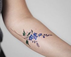 a woman's arm with blue flowers and green leaves on the left side of her arm