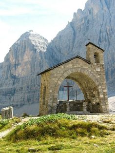 an old stone church with a cross on the front and mountains in the back ground