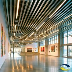 an empty room with large windows and paintings on the wall, along with wooden slats covering the ceiling