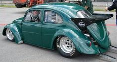 an old green car parked on the side of a road next to a man in a black jacket