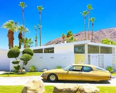 a yellow car parked in front of a white house with palm trees on the side