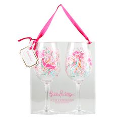 two wine glasses with pink and white designs are in a clear gift box, one has a ribbon on it