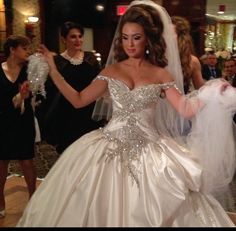 a woman in a wedding dress is walking down the aisle with other people behind her