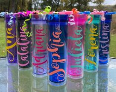 six personalized tumbles sitting on top of a glass table in the sun with ribbons tied to them