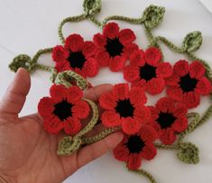 crocheted red and green flowers are being held by someone's left hand