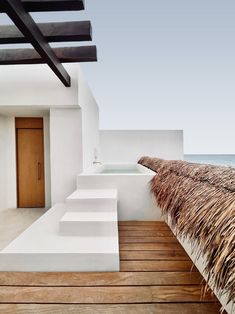 an outdoor bathtub on a wooden deck next to the ocean with thatched roof