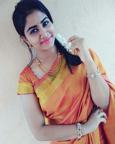 a woman in an orange and yellow sari holding something up to her face while standing next to a wall