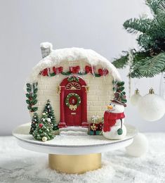 a christmas scene with a small white house and snowman on the top of it