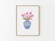 a blue vase filled with pink flowers sitting on top of a white wall next to a wooden frame