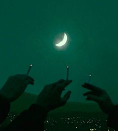 two people holding matchsticks in front of the moon and city lights at night