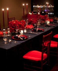 a long table with red flowers and candles on it is set for a formal dinner