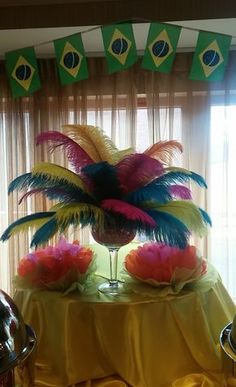 a table topped with a vase filled with colorful feathers and flowers on top of it