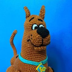 a crocheted stuffed dog with a tag on it's collar, sitting in front of a blue background