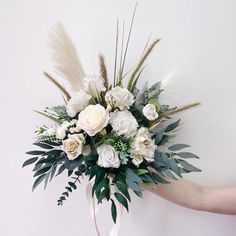 a bouquet of white flowers and greenery is held by someone's hand against a wall