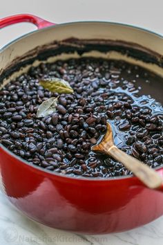 a red pot filled with black beans and a wooden spoon