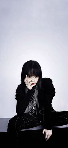 a woman sitting on the ground with her hands to her face and wearing black clothing