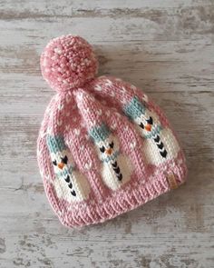 a pink knitted hat with snowmen on it sitting on top of a wooden table