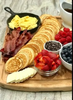 the breakfast is ready to be eaten on the wooden platter with fruit, eggs, bacon and pancakes