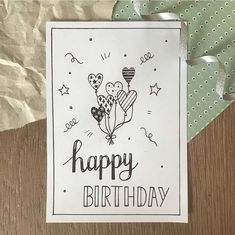 a happy birthday card with hearts and balloons on it, sitting on a table next to some paper