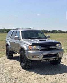 a silver truck parked on top of a dirt road next to a grass covered field