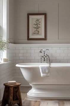 a white bath tub sitting in a bathroom next to a wooden stool and framed artwork