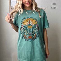 👀Images are an accurate depiction of what you'll receive upon purchase ♂️ All Shirts are Unisex Sizing 👣 Printing is "Direct To Garment"  (Ink printed). Step into a world of enchantment with our Mystical Moth T-shirt. This captivating piece of wearable art combines the timeless allure of folk art with the ethereal vibes of fairycore aesthetics. The graphic on this tee features a majestic moth, its wings adorned with intricate patterns reminiscent of ancient folk art. Surrounding the moth, a ce Green Casual Shirt With Vintage Print, Casual Green Shirt With Vintage Print, Green Vintage Print Short Sleeve Top, Green Short Sleeve Top With Graphic Print, Green Bohemian Top With Graphic Print, Green Top With Graphic Print And Short Sleeves, Vintage Print Relaxed Fit Short Sleeve T-shirt, Relaxed Fit Vintage Print Short Sleeve T-shirt, Relaxed Fit Vintage Print T-shirt