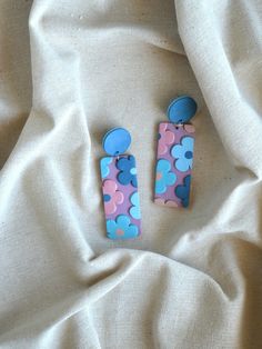 two blue and pink flowered earrings on a white fabric background, one has a button in the middle