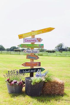 a wooden sign sitting in the middle of a grass field next to potted plants