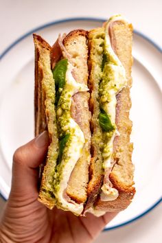 a person is holding a sandwich on a white plate with blue trimmings in their left hand