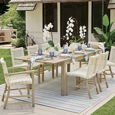 an outdoor dining table with white wicker chairs and blue place mats on a patio