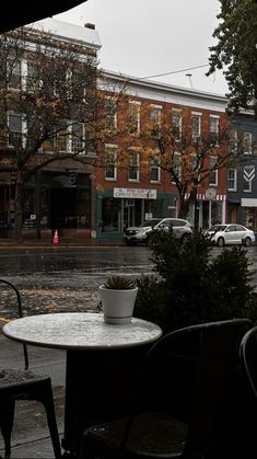 an empty table and chairs on a rainy day in front of a building with cars parked along the street