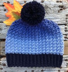 a blue and black knitted hat sitting on top of a wooden bench next to an orange leaf