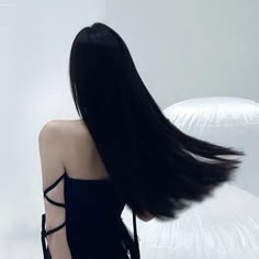 a woman with long black hair standing in front of a white wall and looking back