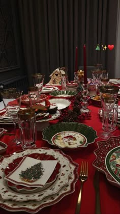 the table is set for christmas dinner with red and green placemats, silverware, and candlesticks