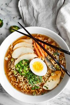 a white bowl filled with noodles, meat and veggies next to chopsticks