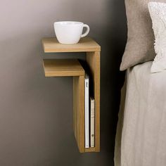 a nightstand with a cup on top of it next to a white pillow and bed