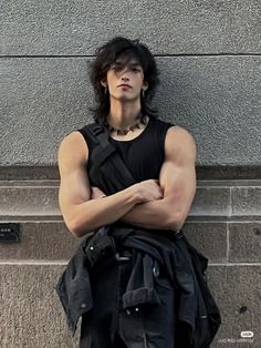 a young man with his arms crossed leaning against a wall wearing a black shirt and leather pants