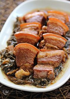 meat and greens in a white dish on a woven place mat with wicker table cloth