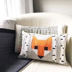 a pillow with an orange fox on it sitting on a white couch next to a window