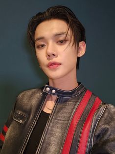 a young man wearing a leather jacket and black shirt with red stripes on his chest