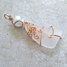 a wire wrapped necklace with white glass beads and gold spirals on the end, sitting on a marble surface