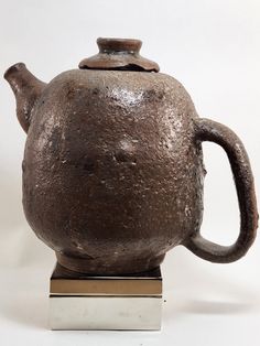 an old teapot sitting on top of a metal stand with a square base in front of it