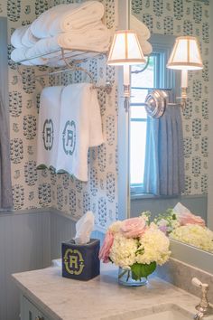 a bathroom with towels hanging on the wall and flowers sitting on the sink counter in front of it