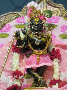 a statue of the hindu god ganesh in pink and gold with flowers around it