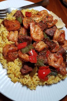 a white plate topped with rice and shrimp next to a fork on a wooden table