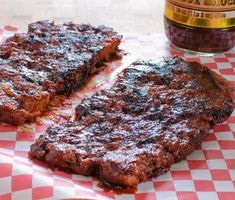 two steaks on a red and white checkered paper with a jar of barbecue sauce in the background