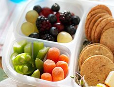 a plastic container filled with crackers, fruit and veggies on top of a table