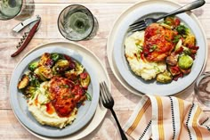 two white plates topped with meat covered in sauce and veggies next to each other