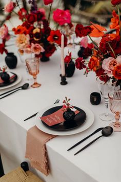 the table is set with black and white plates, silverware, and red flowers