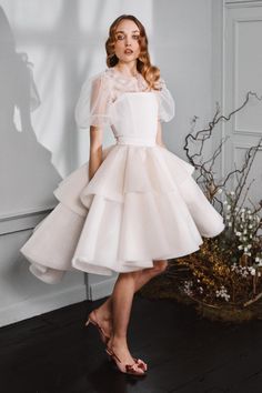 a woman standing in front of a wall wearing a white dress